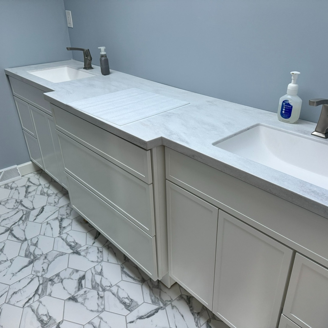 Double-sink bathroom vanity with white shaker cabinets, light gray countertop, and hexagon marble tile flooring.