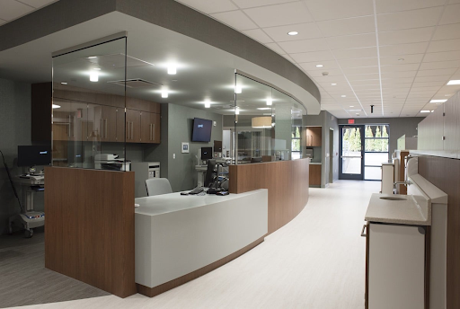 Modern medical office reception area featuring curved wood and white cabinetry, integrated computer workstations, glass partitions, and clean, well-lit patient check-in space designed for durability and hygiene.